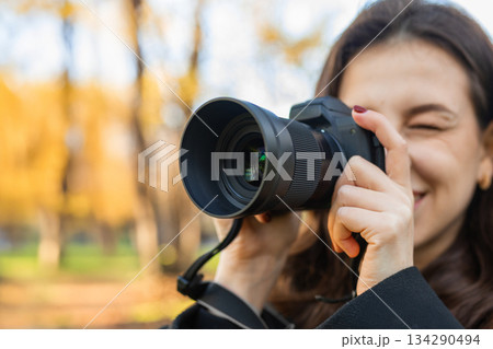 Young woman reviewing photos on her digital camera while standing in a sunny park. Warm autumn light, creative outdoor photography moment, lifestyle scene. 134290494