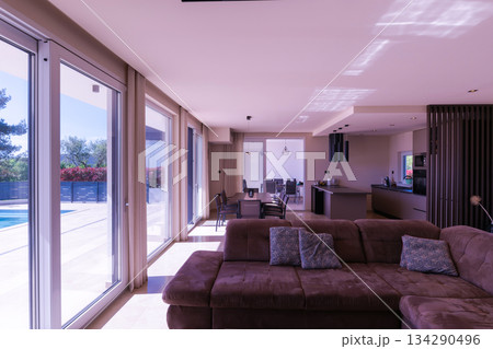 Modern open-plan living and dining room in a luxury villa with large glass doors opening to a private swimming pool, offering a spacious and elegant indoor-outdoor living experience Modern open-plan living and dining room in a luxury villa with large glass doors opening to a private swimming pool, offering a spacious and elegant indoor-outdoor living experience 134290496
