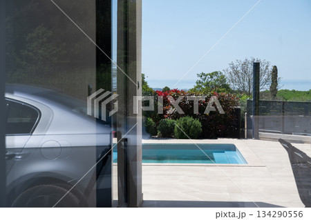Modern home exterior with swimming pool viewed through glass wall, featuring reflections, minimalist design, landscaped garden, and luxury residential architecture in a serene outdoor setting Modern home exterior with swimming pool viewed through glass wall, featuring reflections, minimalist design, landscaped garden, and luxury residential architecture in a serene outdoor setting 134290556