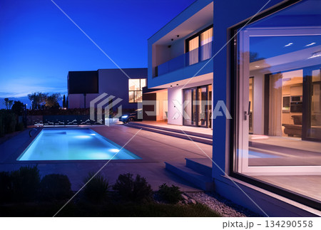 Modern luxury villa with a luminous swimming pool at twilight. Contemporary architecture, sleek design, and inviting interior lights create a serene and elegant evening ambiance, ideal for upscale Modern luxury villa with a luminous swimming pool at twilight. Contemporary architecture, sleek design, and inviting interior lights create a serene and elegant evening ambiance, ideal for upscale 134290558