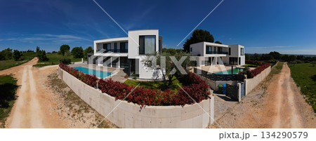 Aerial view of two stunning modern luxury villas with private swimming pools, elegant architecture, and lush green landscaping, set against a beautiful natural backdrop Aerial view of two stunning modern luxury villas with private swimming pools, elegant architecture, and lush green landscaping, set against a beautiful natural backdrop 134290579