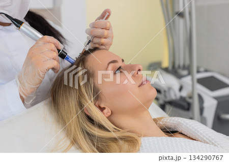 Trichologist doing woman hair regeneration procedure, dermapen microneedling, vitamin injections 134290767