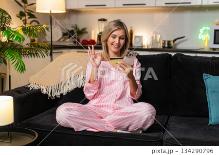 Adult woman confirms online payment on smartphone credit card checks discount smiles saves receipt Adult woman confirms online payment on smartphone credit card checks discount smiles saves receipt 134290796