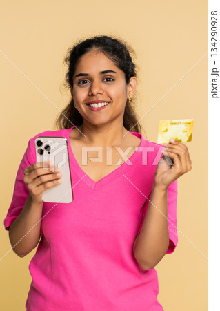 Indian woman holding credit card, focused on smartphone screen, making thoughtful online purchase 134290928
