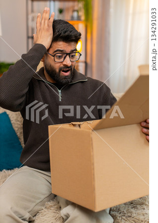 Indian man on sofa opens box and shakes head after discovering wrong item in online delivery order Indian man on sofa opens box and shakes head after discovering wrong item in online delivery order 134291033
