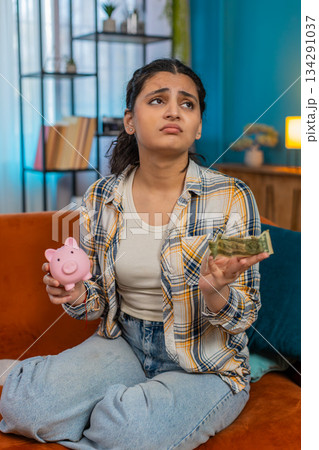 Woman sadly looking at piggy bank with one dollar inside financial difficulties limited savings Woman sadly looking at piggy bank with one dollar inside financial difficulties limited savings 134291037