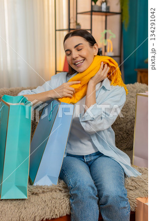 Young woman on home sofa happily unpacking new clothes from shopping bag joyfully examining purchase Young woman on home sofa happily unpacking new clothes from shopping bag joyfully examining purchase 134291042