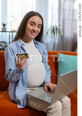 Online shopping buying pregnant woman sitting on home sofa making purchase using laptop credit card Online shopping buying pregnant woman sitting on home sofa making purchase using laptop credit card 134291188