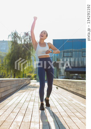 Athletic runner woman looks at smartwatch device fitness bracelet checking heart rate in city park Athletic runner woman looks at smartwatch device fitness bracelet checking heart rate in city park 134291192