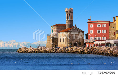 A view of Our Lady of Health Church in the old Slovenian town of Piran. Cityscape of Piran with snowy mountains in the background A view of Our Lady of Health Church in the old Slovenian town of Piran. Cityscape of Piran with snowy mountains in the background 134292599