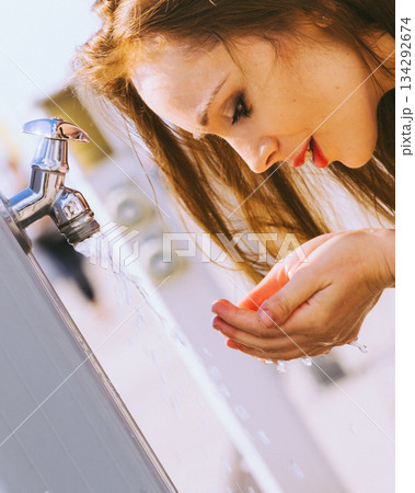 Woman drinking water from street tap Woman drinking water from street tap 134292674