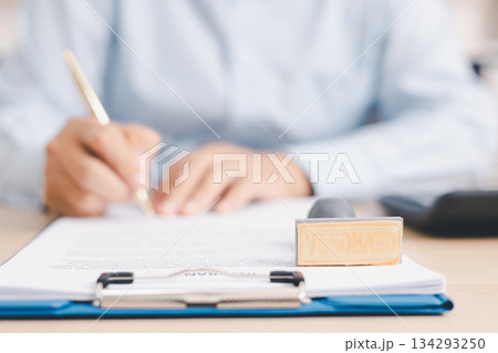 Businessperson stamping document on clipboard at office desk, concept of contract approval, legal authorization, business agreement validation or administrative paperwork process. stamp approval. 134293250