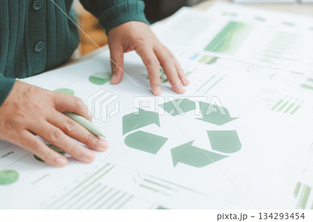 Business person holding recycle symbol on clipboard with green charts on desk, representing circular economy, eco responsibility, sustainability and environmental business concept. 134293454