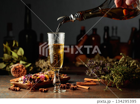 Yellow herbal liquor or mixture is poured from a vintage bottle into a glass. 134295395