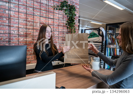 Friendly shop assistant handing paper bag to customer in secondhand store 134296063