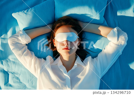 Above view of woman wearing yellow shirt with eye mask sleeping in bed. Above view of woman wearing yellow shirt with eye mask sleeping in bed. 134296710