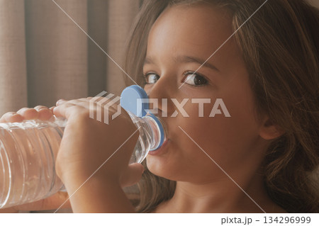 Candid close-up: child drinking from a disposable water bottle on a sunny day 134296999