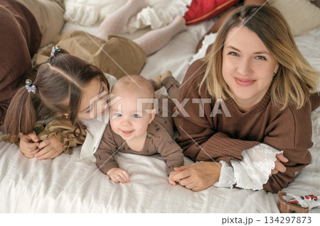 Funny laughing infant kid next to his mother and sister lying on the bed looking at the camera. Funny laughing infant kid next to his mother and sister lying on the bed looking at the camera. 134297873