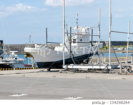 Fishing boat undergoing maintenance on a dry dock in a sunny harbor with blue sky and clouds Fishing boat undergoing maintenance on a dry dock in a sunny harbor with blue sky and clouds 134298264
