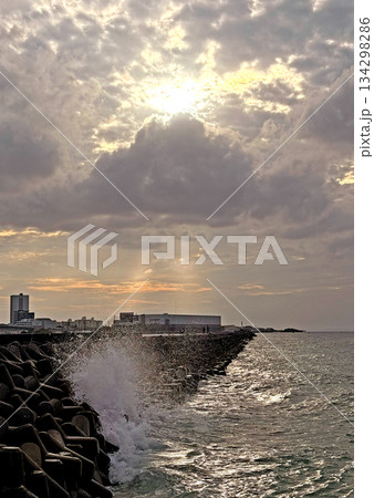 Dramatic sunset over industrial coastline with crashing waves against tetrapods Dramatic sunset over industrial coastline with crashing waves against tetrapods 134298286