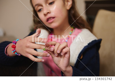 Young Girl Admires a Green Ring While Trying On Jewelry, Beaded Bracelets On Display 134301742