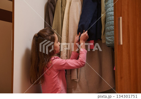 Little Girl Selecting Clothes From Closet With Coats In A Pink Shirt For A Warm Wardrobe Moment 134301751