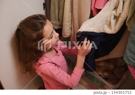 Young Girl Exploring a Closet of Coats and Jackets in a Cozy Home Setting Young Girl Exploring a Closet of Coats and Jackets in a Cozy Home Setting 134301752