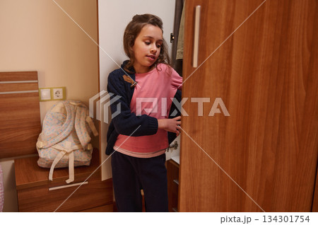 Young Girl In Pink Shirt Explores Open Closet In Cozy Bedroom 134301754