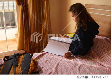 Young Student Studying On Bed With Notebook And Backpack Ahead Of Travel Young Student Studying On Bed With Notebook And Backpack Ahead Of Travel 134301757