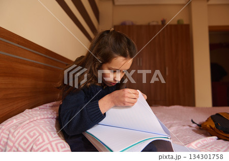 Young Girl Reading a Notebook on Bed, Concentrated Moment of Study and Quiet Learning 134301758