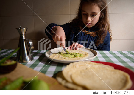Young Girl Preparing Homemade Flatbread With Guacamole At Family Kitchen Table 134301772