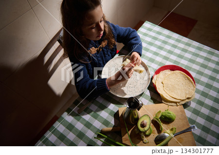 Young Girl Enjoying Breakfast With Pancakes, Avocado, and Fresh Bread at Table 134301777