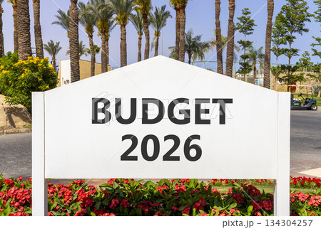 Budget 2026 symbol. Concept words Budget 2026 on beautiful white road sign. Beautiful palm trees palm-trees and blue sky background. Business and budget 2026 concept. Copy space. 134304257