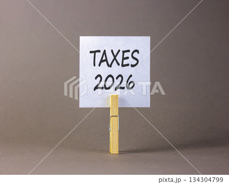 Taxes 2026 new year symbol. Concept words Taxes 2026 on beautiful white paper on wooden clothespin. Beautiful grey background. Business and taxes 2026 new year concept. Copy space. Taxes 2026 new year symbol. Concept words Taxes 2026 on beautiful white paper on wooden clothespin. Beautiful grey background. Business and taxes 2026 new year concept. Copy space. 134304799