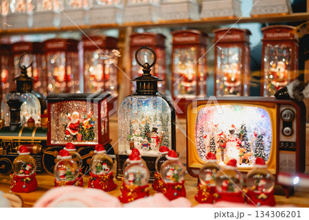 A collection of illuminated Christmas snow globes shaped like a train, TV, and telephone booths at a festive holiday market. A collection of illuminated Christmas snow globes shaped like a train, TV, and telephone booths at a festive holiday market. 134306201