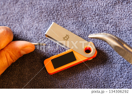 Light-skinned man tampering with hardware wallet with tools indoors Light-skinned man tampering with hardware wallet with tools indoors 134306292