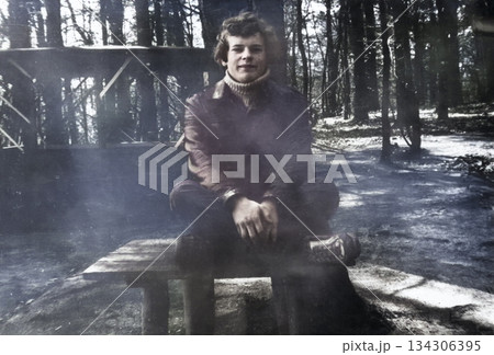 Vintage portrait of a handsome sixteen-year-old blond boy sitting on a bench in the woods on vacation. Retro photo, 1982. Vintage portrait of a handsome sixteen-year-old blond boy sitting on a bench in the woods on vacation. Retro photo, 1982. 134306395