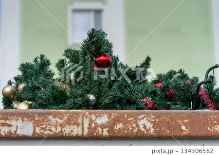 Discarded plastic fir trees decorated with red Christmas balls in a trash container. 134306582