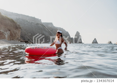 Woman swimming inflatable in ocean, happy person enjoying summer beach vacation with cliffs in background 134307014