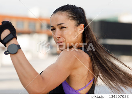 Woman doing high-intense warming up. High detailed portrait of a muscular athlete practicing punches outdoors. 134307028