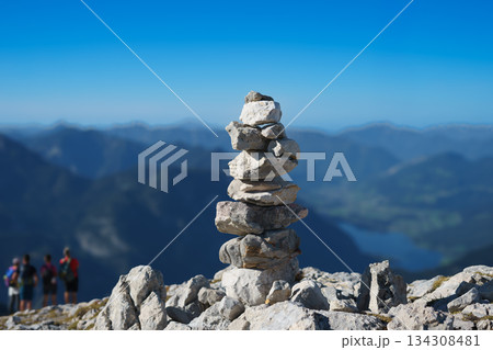 Stone pyramid in the mountains on the top, laid out on a hiking trail against the backdrop of the Alps and blue sky 134308481