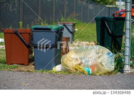 Household trash bins and a plastic garbage bag placed outdoors along a suburban street, illustrating waste management, recycling issues, and pollution 134308490