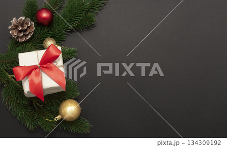 White gift box with twine, pine branches, frosted cone and gold ornaments on dark background, festive and elegant 134309192