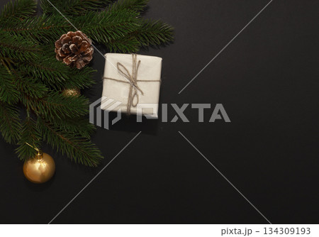 White gift box with twine, pine branches, frosted cone and gold ornaments on dark background, festive and elegant 134309193