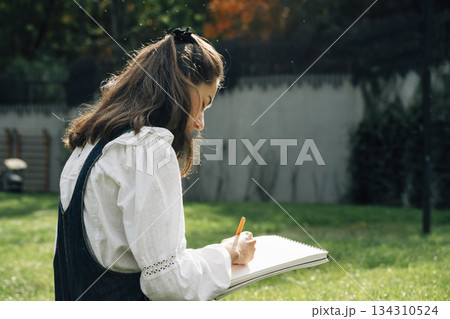 Girl Drawing in Summer Park. Relax lifestyle portrait Girl Drawing in Summer Park. Relax lifestyle portrait 134310524
