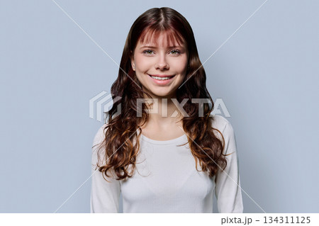 Portrait of smiling teenage girl with curly long hair on gray background 134311125