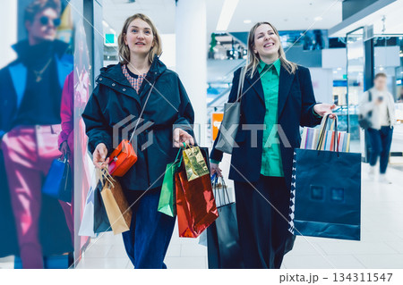 Two happy women leaving store after shopping with colorful shopping bags in their hands 134311547