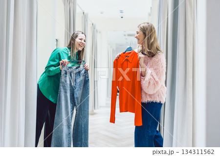 Two women shopping in store trying on clothes in fitting room 134311562