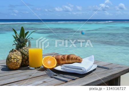 Fresh Tropical Breakfast Setup on Beachside with Pineapple, Juice, and Croissant 134316727