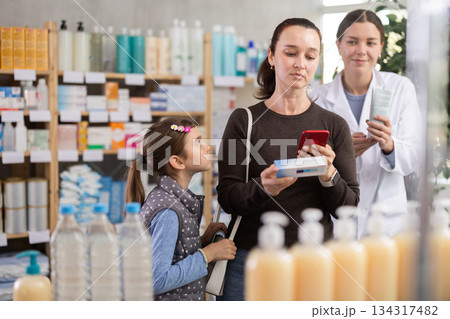Woman using phone to check ingredients of ointment with pharmacist guidance Woman using phone to check ingredients of ointment with pharmacist guidance 134317482